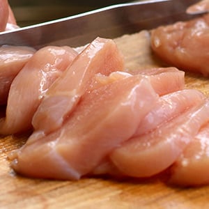 Sliced, raw chicken breast on a cutting board.